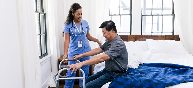 Home health nurse helping man use walker